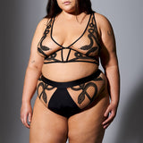 size 1x/2x white model wearing a skin toned tattoo style longline bralette and high waisted bikini panty both pieces with gorgeous snake embroidery