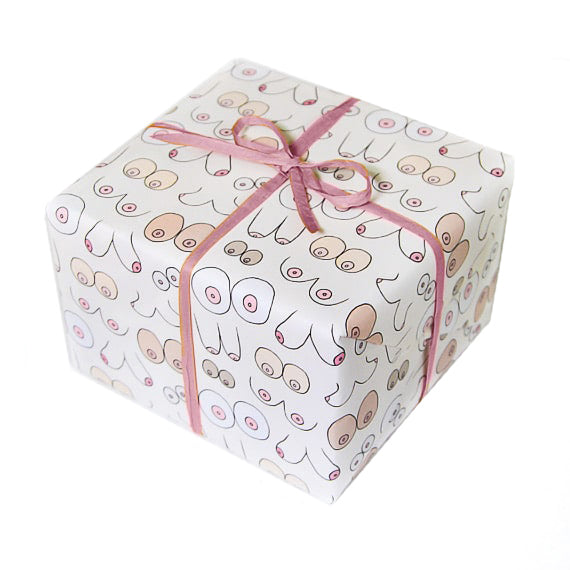 A square gift is wrapped in wrapping paper with white background and boob outlines in different shapes, sizes, and colors. Tied with a pink bow on top